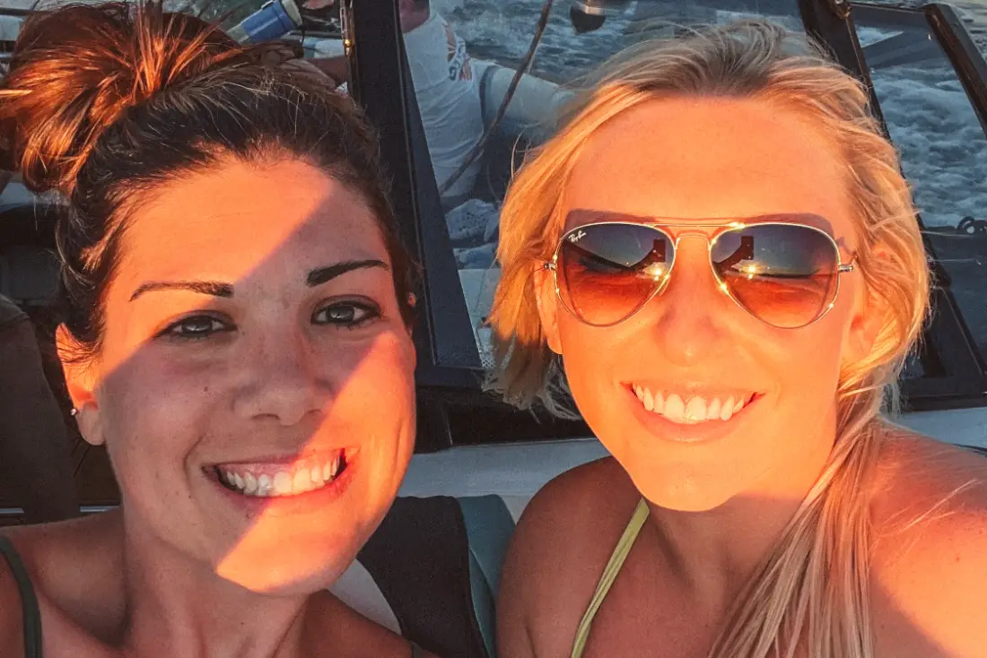 Girls having fun during a public wakesurfing charter while someone surfs on Lake Winnipesaukee.